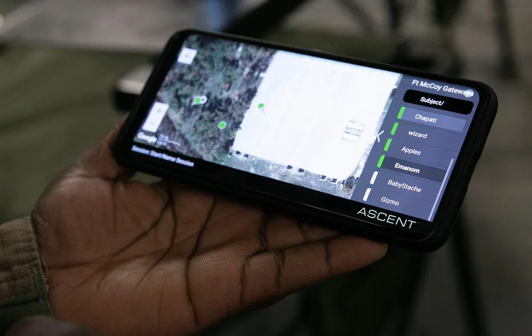 A soldier holding a phone in the field running the ASCENT platform, showing a satellite map with tracked subjects